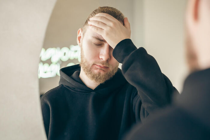 Man in black hoodie looking stressed holding his forehead reflecting on toxic traits