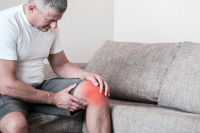 A man clutching his knee with a red highlight, indicating pain from an extreme illness or sickness.