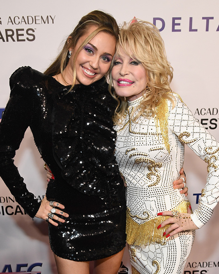 Miley Cyrus and Dolly Parton smile, arm-in-arm, at an event. Miley's announcement sparks fury after Parton's passing.