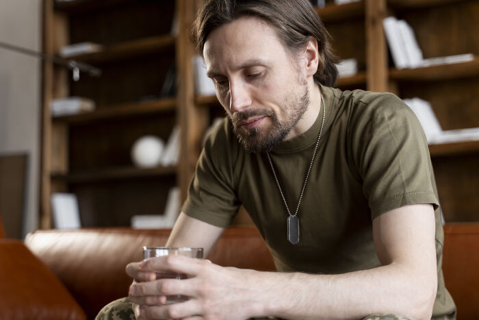 A man in a military uniform holds a glass, looking downcast, reflecting parents' concern for their children.