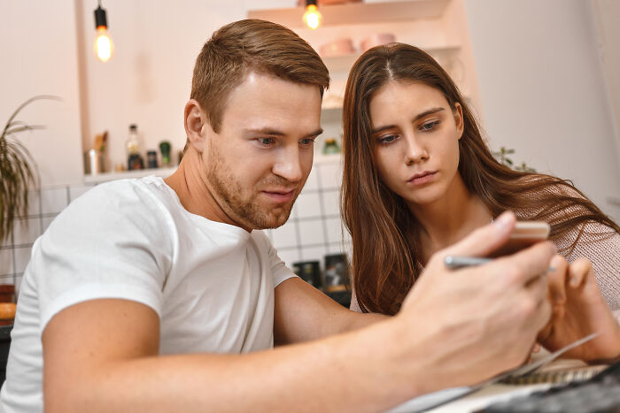 Serious young couple looking at phone together, discussing marriage regrets