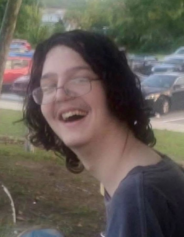 A young man with long dark hair, glasses, and a mustache smiling, the missing son.