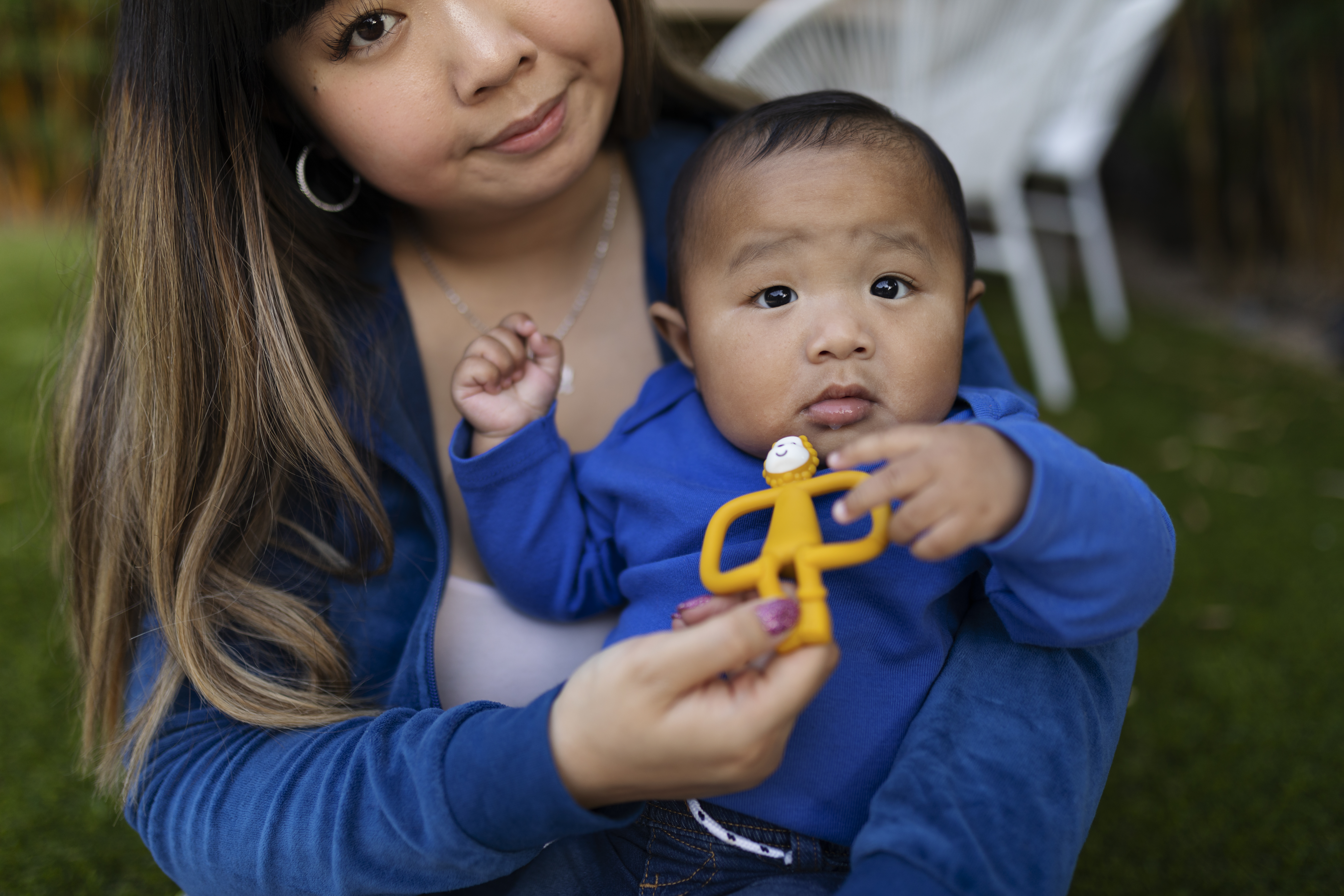 Young woman holding a baby in blue outfit playing with a toy outside