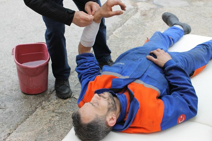 A person bandaging another person's arm on the ground, depicting an injury that might lead to legal excuses.