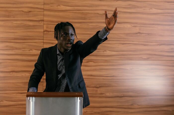 A man speaking at a podium with his hand raised, symbolizing ridiculous legal excuses in court.