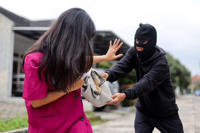 A masked person attempting to snatch a bag from a woman. This image illustrates legal excuses.