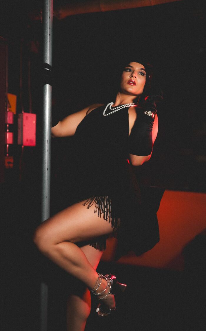 A woman in a black flapper dress and pearls posing next to a pole. This image illustrates legal excuses.
