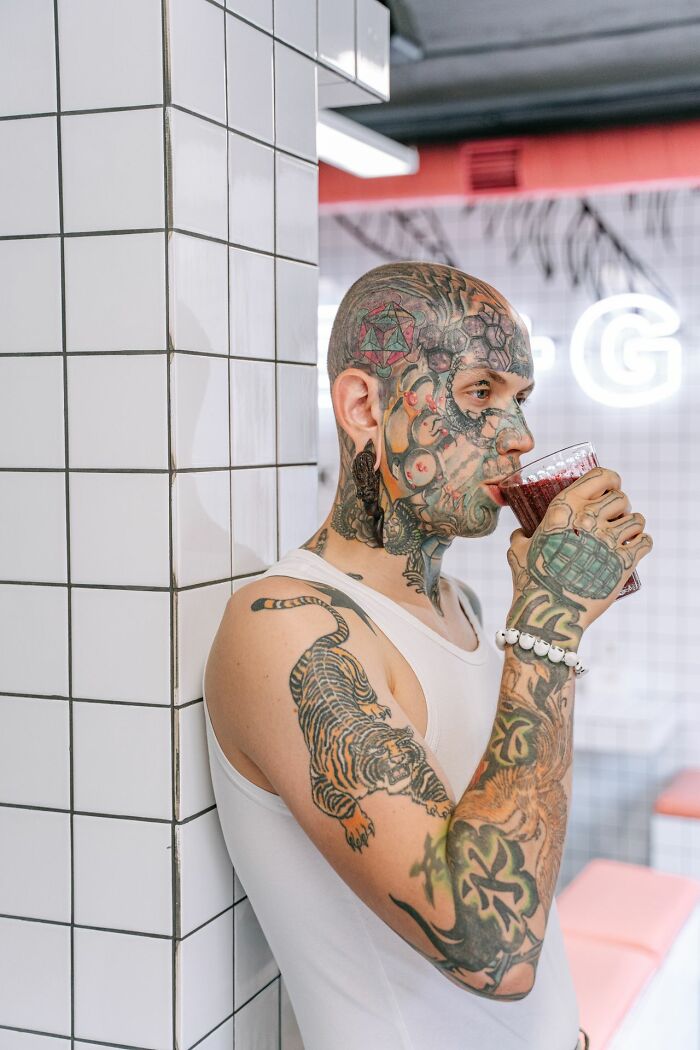 A heavily tattooed man drinks from a glass, perhaps considering his legal excuses.