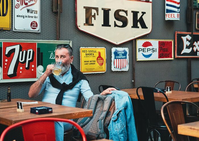 A man drinks beer at a cafe with vintage signs; a legal excuse might relate to a public intoxication charge.