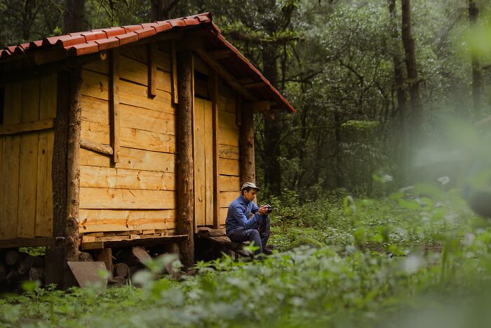 A man sitting by a rustic cabin in the woods, reflecting on a midlife crisis.