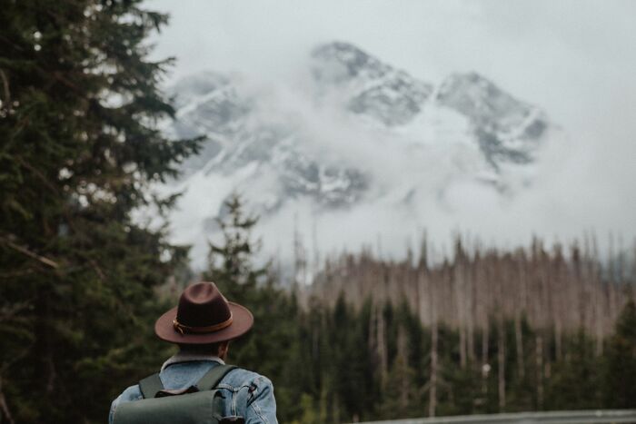 A person with a hat and backpack looking at a mountain range, depicting a midlife crisis journey.