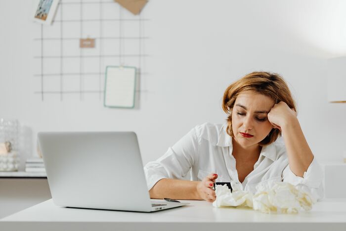 A woman looking tired while working on a laptop, perhaps overwhelmed by a midlife crisis.