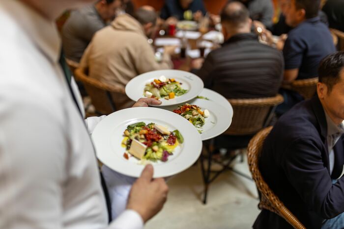 A waiter serving salads to people, possibly experiencing a midlife crisis and making lifestyle changes.