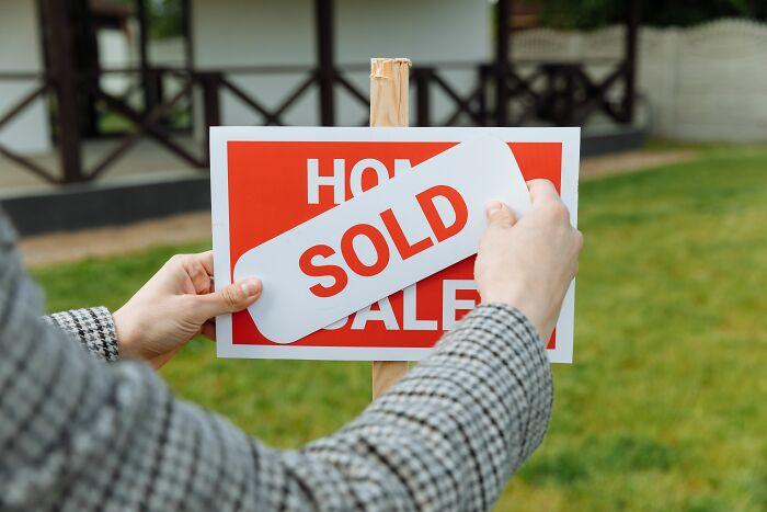 Hands place a SOLD sign over a FOR SALE sign, possibly reflecting a midlife crisis decision.