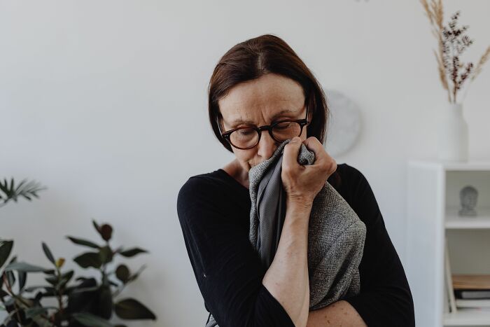 A woman with glasses smells a gray piece of fabric, a sign of her unhinged midlife crisis.