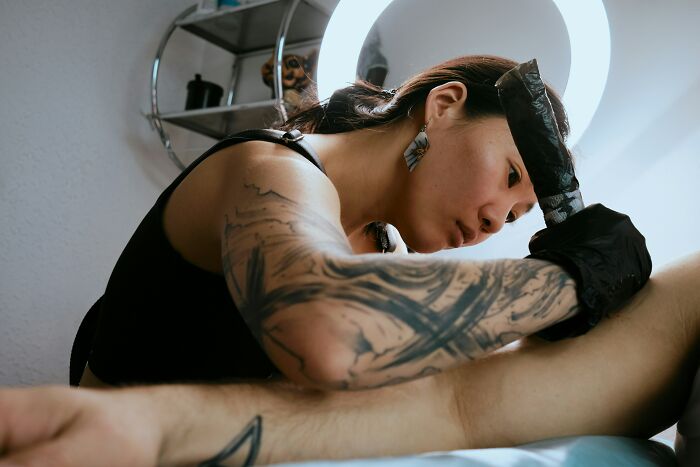 A tattoo artist with tattooed arms works on a client, an unhinged choice for a midlife crisis.