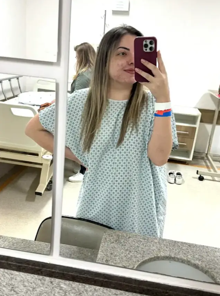 A young woman in a hospital gown taking a mirror selfie, showing her strength.