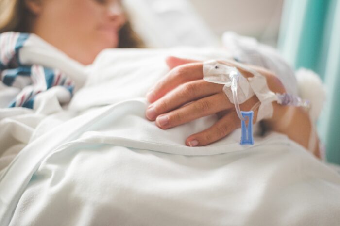 A close-up of a patient's hand with an IV drip in a hospital bed, a reminder of when they passed away.