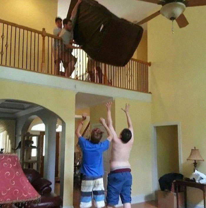 Group dropping couch dangerously from second-floor balcony inside house