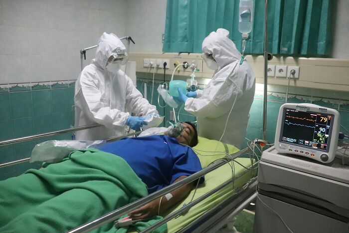 Medical professionals in PPE tend to a patient on a stretcher, showing extreme illness and sickness.