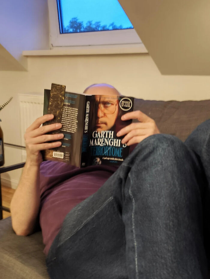 Hilarious photos: A man on a couch reading a book, only his eyes and the book cover are visible.