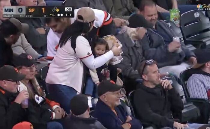 Mom serving food and holding baby at Giants baseball game