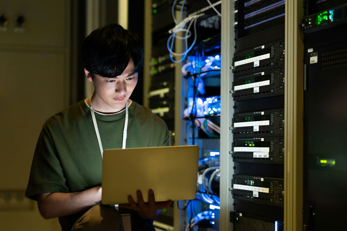 A man working on a laptop in front of server racks, symbolizing AI infrastructure near endangered animals.