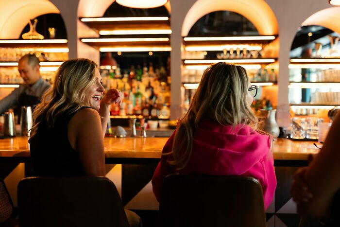 Two women at a bar, one laughing, illustrating social situations where clients might make regrettable statements to the cops.
