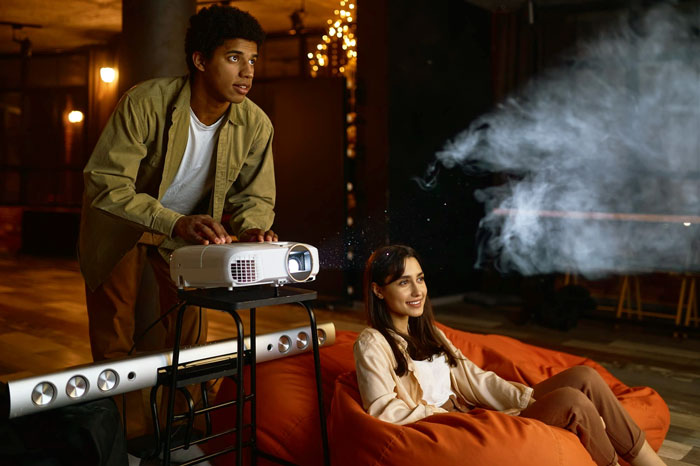 A man adjusting a projector next to a woman on a bean bag chair during a movie night A man adjusting a projector next to a woman on a bean bag chair during a movie night