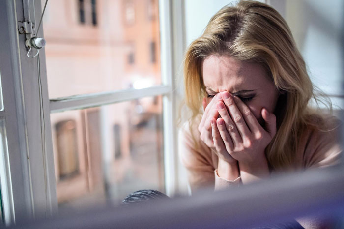 A distraught woman crying by a window, hands covering her face. Neighbors ignore warnings about their dogs attacking her cat. A distraught woman crying by a window, hands covering her face. Neighbors ignore warnings about their dogs attacking her cat.