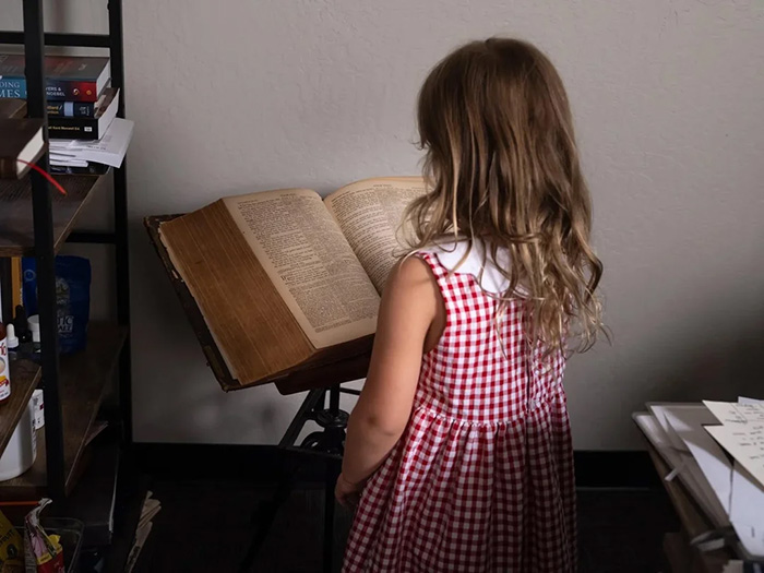 A young girl in a red and white checkered dress looking at a large open book on a stand A young girl in a red and white checkered dress looking at a large open book on a stand