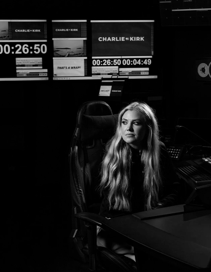 A black and white Erika Kirk photo showing her seated in a dimly lit studio environment A black and white Erika Kirk photo showing her seated in a dimly lit studio environment