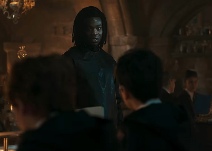 A Black Harry Potter actor standing amidst a dimly lit room with other students in the foreground, looking serious. Harry Potter backlash. A Black Harry Potter actor standing amidst a dimly lit room with other students in the foreground, looking serious. Harry Potter backlash.