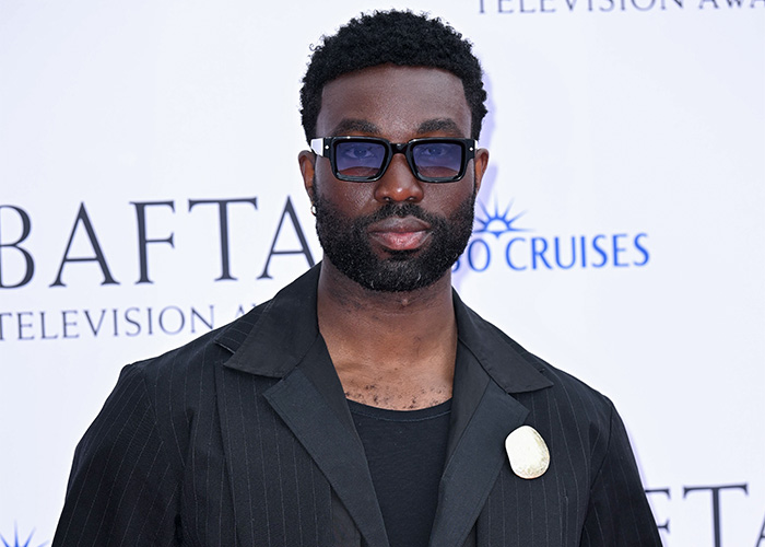A Black Harry Potter actor with a beard, wearing sunglasses and a dark suit jacket, posing on a red carpet. Harry Potter backlash. A Black Harry Potter actor with a beard, wearing sunglasses and a dark suit jacket, posing on a red carpet. Harry Potter backlash.