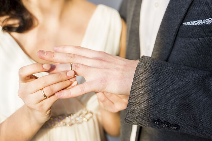 A person's hands placing a wedding ring on another's finger, relating to childhood beliefs about marriage.