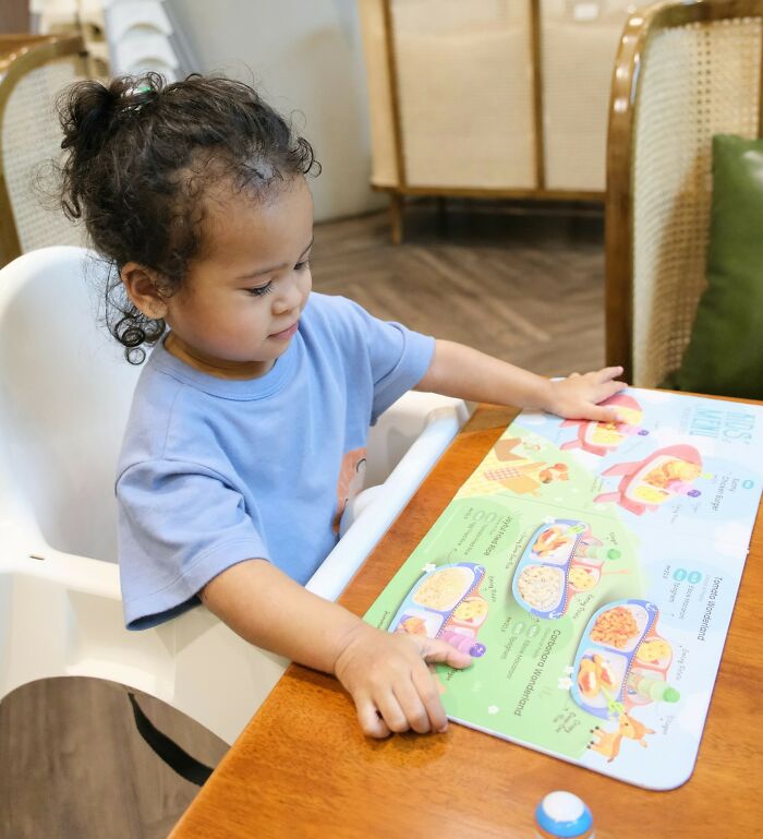 A toddler in a high chair looking at a colorful book, an action some people judge others for.