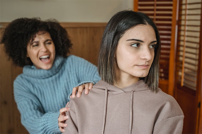 A woman looking displeased as her friend yells behind her, illustrating unsolicited bikini advice and body-shaming. A woman looking displeased as her friend yells behind her, illustrating unsolicited bikini advice and body-shaming.