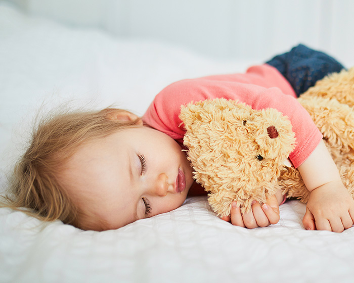 A baby sleeping peacefully with a teddy bear, illustrating a child's rest in a nursery.