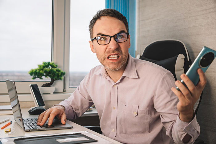 An angry employee at his home office with a laptop and phone, feeling frustrated about the remote work policy. An angry employee at his home office with a laptop and phone, feeling frustrated about the remote work policy.