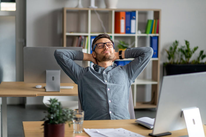 An employee at his home office, relaxing with hands behind his head. His approved home office setup is visible with a computer. An employee at his home office, relaxing with hands behind his head. His approved home office setup is visible with a computer.