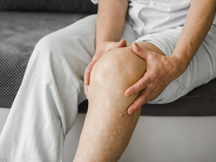 A person holding their knee in pain, a common health symptom that terrifies doctors.