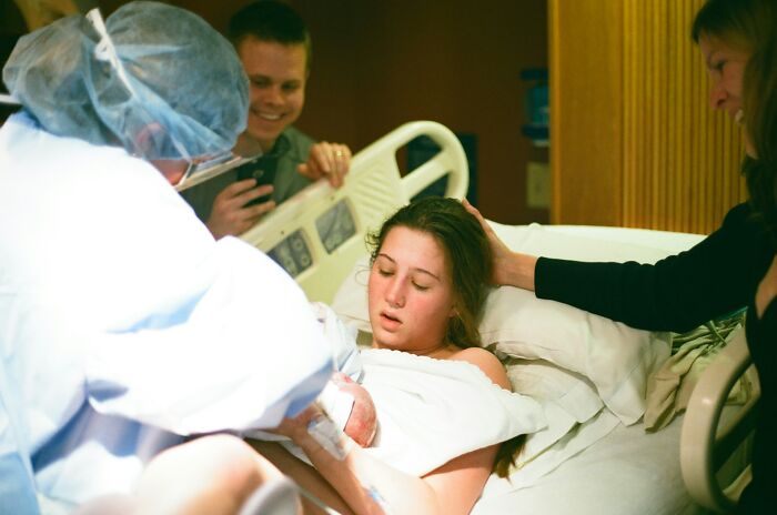 A woman giving birth in a hospital bed surrounded by family, a key moment in medical practices.
