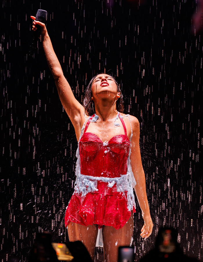 Olivia Rodrigo raising her arm holding a microphone while wearing a red dress with melting effects on tour Olivia Rodrigo raising her arm holding a microphone while wearing a red dress with melting effects on tour