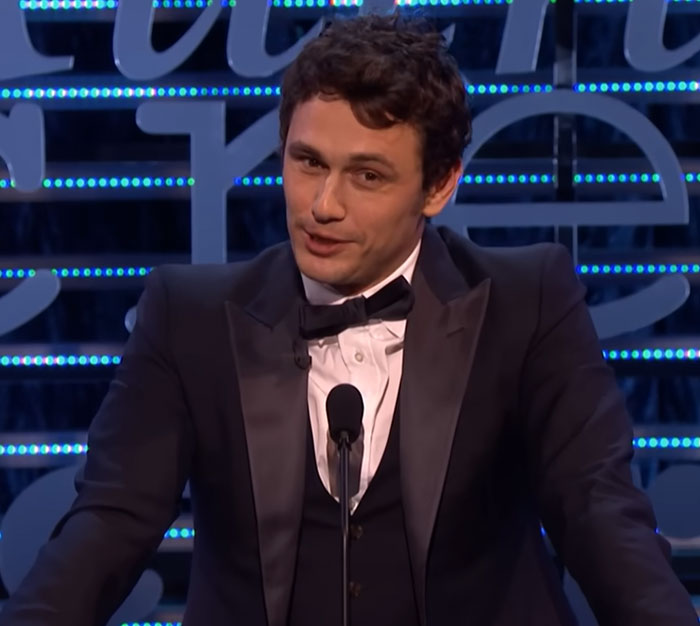 Actor James Franco smiling at a podium, an example of celebrities making unexpected appearances.
