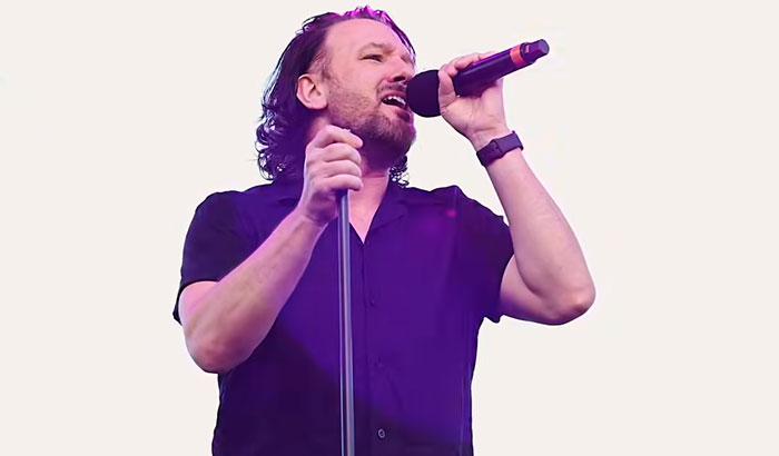 A photo of singer Peter Hook performing live on stage, illustrating stories of celebrities.
