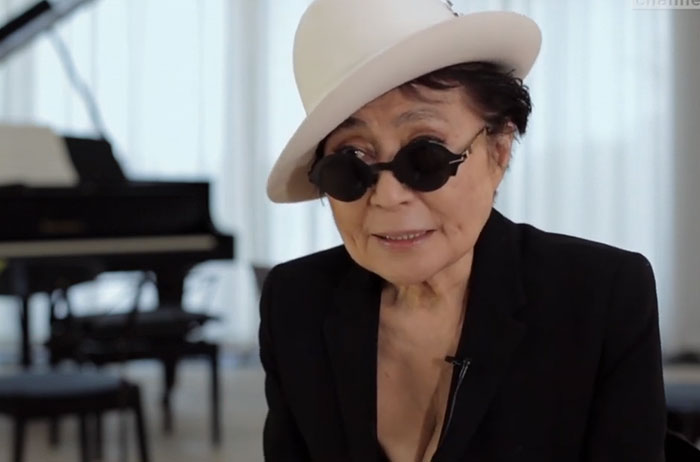 Yoko Ono, among the celebrities who met ordinary people, wearing a white hat and sunglasses next to a piano