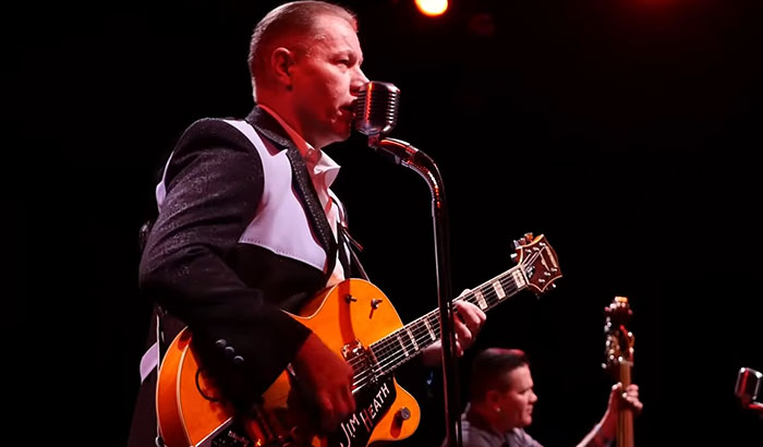 Musician Jim Heath playing guitar on stage, showcasing famous celebrities.