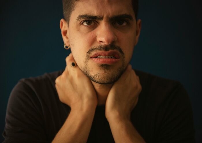 A man with a distressed expression, hands on his neck, depicting men's unhinged lies.