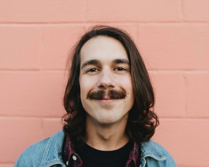 Man with long hair and mustache smiling, embodying one of the things people do that others judge them for.