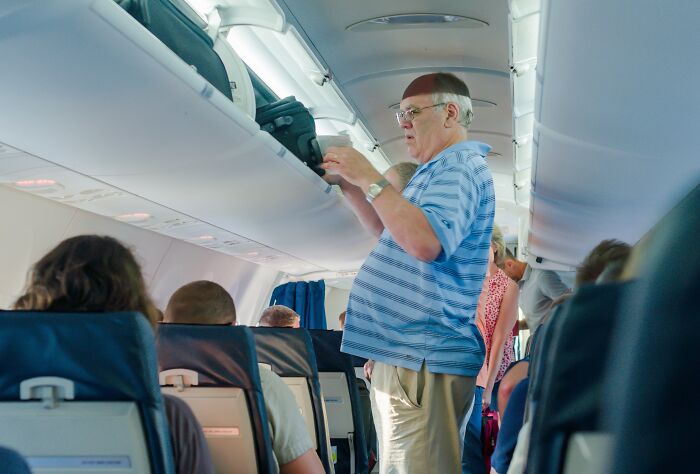 A passenger stowing luggage in the overhead bin on an airplane, illustrating a passenger action that flight attendants might dislike.